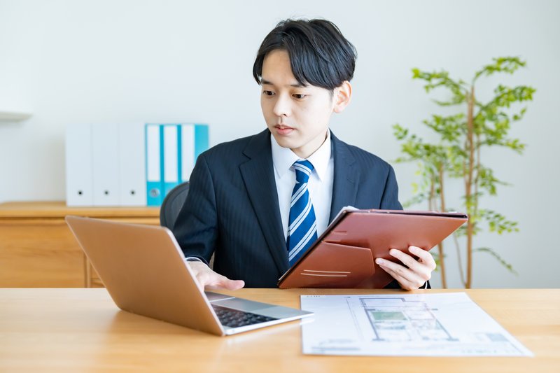 間取り図とタブレットで作業する不動産担当者(M)