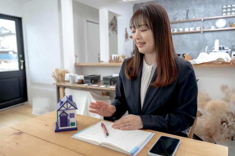 不動産会社のデスクで相談する女性（家の模型）